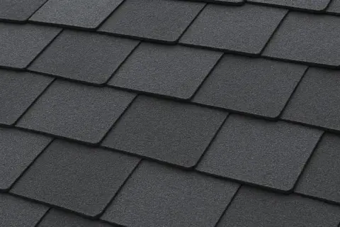 Close-up of dark grey, textured recycled shingles on a roof, showcasing their layered pattern and durable appearance.