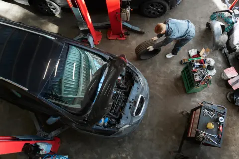Mechanik w warsztacie samochodowym trzyma oponę obok podniesionego samochodu i skrzynki z narzędziami.