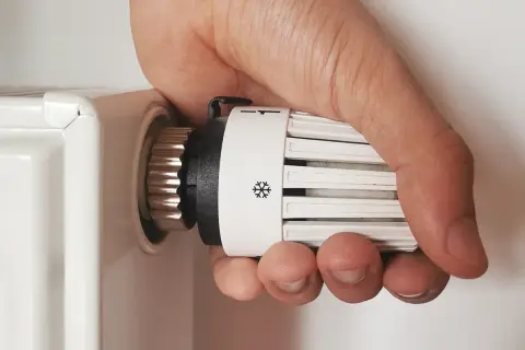 Regolare valvole termostatiche stanza per stanza: mano che gira la manopola del termosifone per impostare la temperatura desiderata.