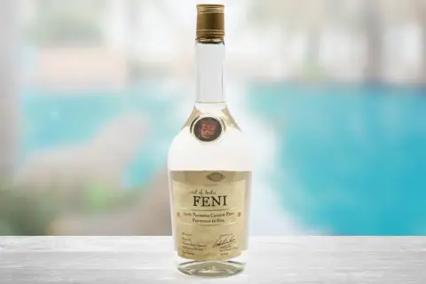 Butelka Feni, indyjskiego alkoholu z nerkowców, na tle basenu.