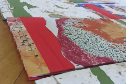 Dettaglio di come rilegare fogli a mano con filo, creando un quaderno artistico con copertina colorata.