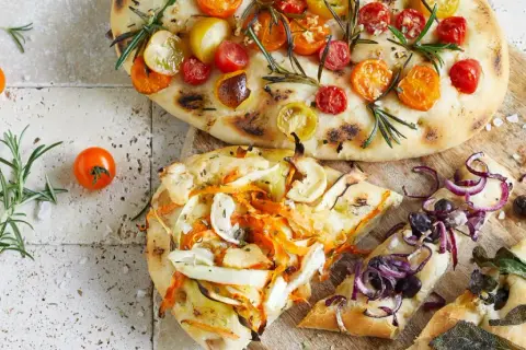 Zwei Focaccias mit Tomaten, Gemüse und Zwiebeln, garniert mit Rosmarin und Salbei.