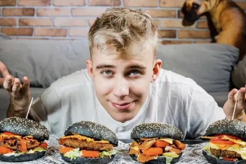 Młody mężczyzna prezentuje cztery burgery w ramach porównania burgerów od znanych youtuberów. Który jest najlepszy?