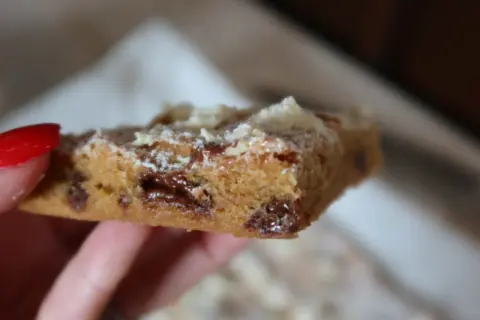 En hand håller en bit av ett blondie recept med chokladbitar.