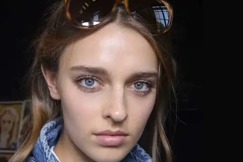 Ragazza con occhiali da sole in testa, viso illuminato da fondotinta e fard, ciglia lunghe e occhi azzurri.