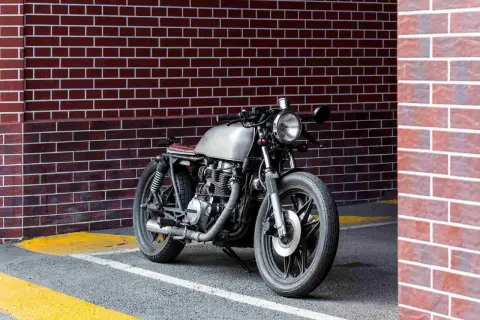 Stylowy motocykl miejski z metalicznym bakiem i brązowym siedzeniem stoi przy ceglanej ścianie.