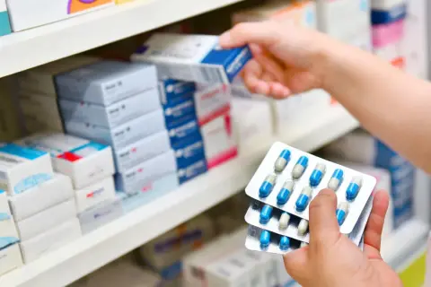 Ręka farmaceuty wybiera z półki lek, w tym antybiotyk azytromycyna w blistrach.
