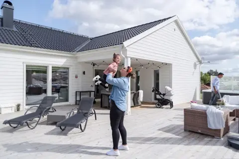 En kvinna lyfter sitt barn på en altan vid ett modernt hus, en idyllisk semesterbild från ett resort i Sverige.