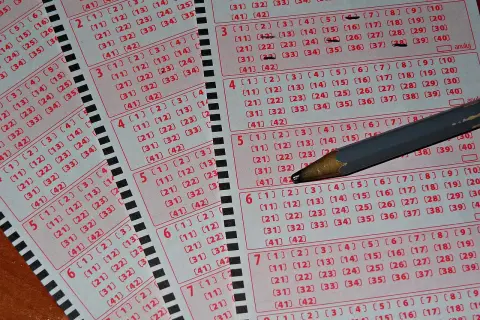 Kaskada kuponów lotto z zaznaczonymi liczbami i ołówkiem. Tabela wygranych czeka na szczęśliwców.