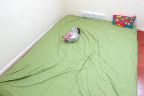 A baby sleeps on a green mattress on the floor, a simple setup for how to make a floor bed for baby. A colorful map pillow rests nearby.