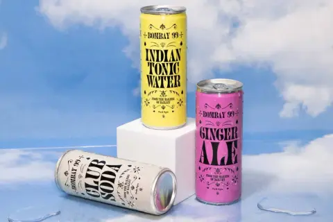 Three Bombay 99+ cans: Club Soda, Indian Tonic Water, and Ginger Ale, styled by Jessica Walsh, against a sky backdrop.