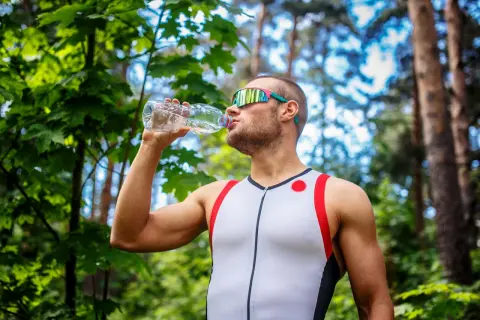 Mężczyzna w sportowym stroju pije wodę z butelki, co pić podczas treningu w plenerze.