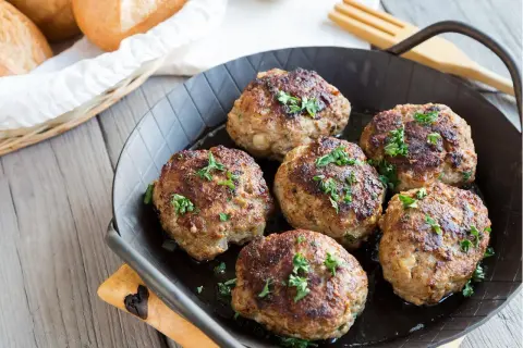 Sechs goldbraune Fleischpflanzerl, frisch aus der Pfanne, garniert mit Petersilie. Ein leckeres Fleischpflanzerl Rezept zum Nachkochen.
