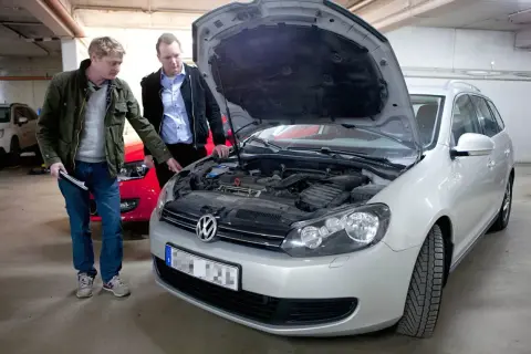 Två män inspekterar motorutrymmet på en silverfärgad kombi. En av dem pekar mot motorn, kanske för att diskutera kamremmen på 1.4 TSI-motorn.