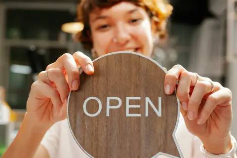 Frau hält ein Holzschild mit der Aufschrift "OPEN" in einem Café.