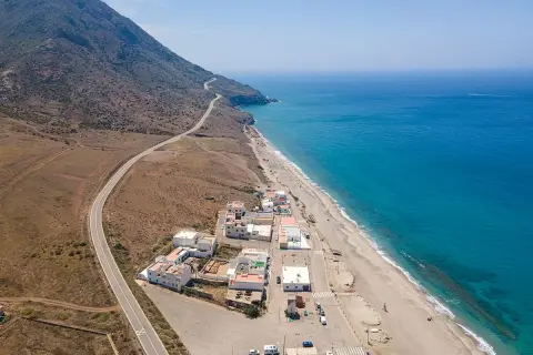 Vista aérea de la playa de la Almadraba en Almería, con el mar azul intenso, la arena dorada y un pueblo costero.