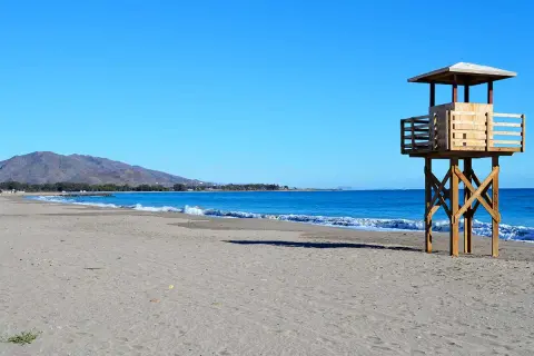 Torre de vigilancia de madera en la playa de Vera, con arena y mar azul. La playa de Vera tiene piedras, pero hoy el sol brilla.