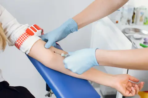 Pobieranie krwi do badań na czczo. Pielęgniarka w rękawiczkach pobiera krew z żyły pacjentki.