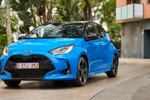 Błękitna Toyota Yaris 1.3 benzyna zaparkowana na tle zieleni i budynku. Zastanawiasz się, jaki olej do toyoty yaris 1.3 benzyna?