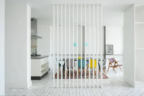 Elegante divisor vertical para dividir salón en dos ambientes, separando la cocina de la zona de comedor con sillas de colores.