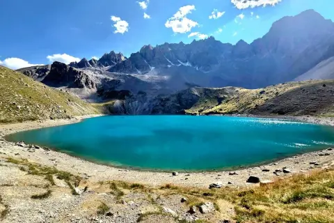 Magnifique lac Saint-Anne aux eaux turquoise, entouré de montagnes rocheuses et de pentes herbeuses sous un ciel bleu éclatant.