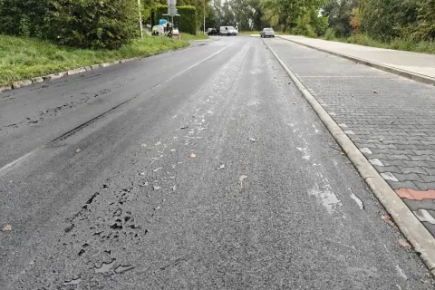 Droga w Cieszynie po deszczu, z kałużami na asfalcie i nowym chodnikiem z kostki.