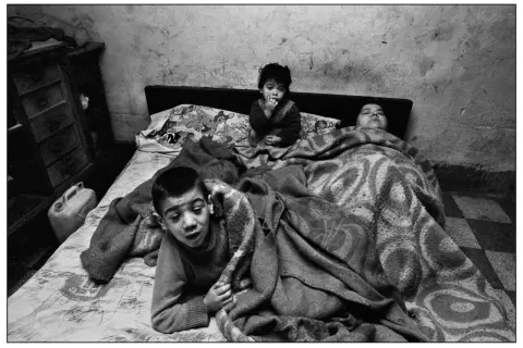 Bambini in un letto, un piccolo è seduto con le dita in bocca, un altro è sdraiato. Un'immagine toccante, una delle **Letizia Battaglia foto famose**.