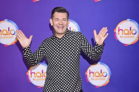 Zenek Martyniuk w czarno-białej koszuli w grochy, z podniesionymi rękami, na tle fioletowym z logo "halo tu Polsat".