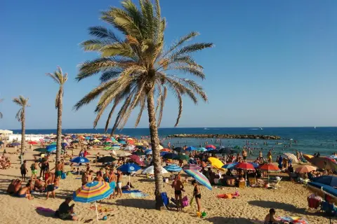 Spiagge Marina di Ragusa affollate di bagnanti sotto palme e ombrelloni colorati, con il mare azzurro sullo sfondo.
