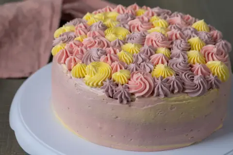 En vacker tårta med rosa, lila och gula frostingrosor. Denna tårta är perfekt för att spritsa tårta till ett speciellt tillfälle.