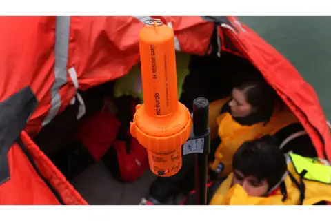 Arancione transponder navi SART McMurdo in una zattera di salvataggio con persone con giubbotti di salvataggio.