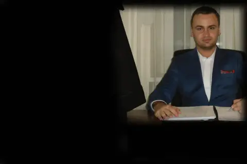 Mężczyzna w garniturze siedzi przy biurku z dokumentami.