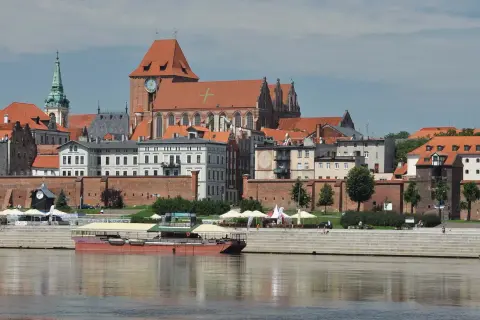 Widok na średniowieczny zespół miejski Torunia z Wisłą w tle. Zabytkowe kamienice i kościół tworzą malowniczą panoramę.