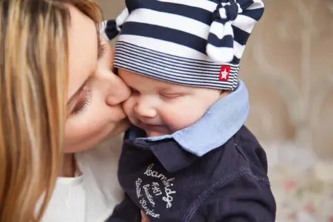 Czuła matka całuje dziecko w czapeczce. Pokazuje to sposoby radzenia sobie ze złością u dzieci, poprzez miłość i bliskość.