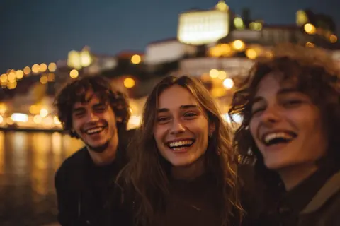 Tre amici ridono felici, immersi nella magica atmosfera del porto vita notturna, con le luci sfocate della città a fare da sfondo.