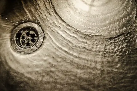 Acqua che scorre su uno scarico metallico, un'immagine che evoca il processo di come sciogliere il grasso nei tubi di scarico.