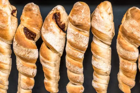 Goldbraunes Stockbrot ohne Hefe, mit dunkler Füllung, auf schwarzem Hintergrund.