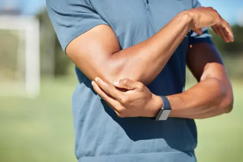 Mężczyzna trzyma się za bolący łokieć, nosząc zegarek sportowy.