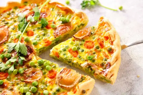 Un delicioso quiche de verduras, con guisantes, zanahoria y trozos de queso dorado, recién cortado y listo para servir.
