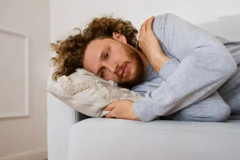 Uomo con capelli ricci e barba sdraiato su un divano, che riflette sulla necessità di esercizi per superare l'agorafobia.