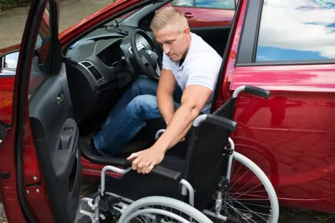 Mann mit Rollstuhl steigt in rotes Auto. Dies illustriert die behinderungsbedingte Fahrtkostenpauschale.