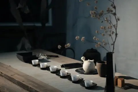 Service à thé minimaliste avec tasses blanches alignées. Une théière en céramique et un vase de fleurs séchées évoquent l'art de comment conserver le thé.