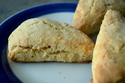Tre gyllene scones, bakade med bakpulver, ligger på en tallrik med blå kant.