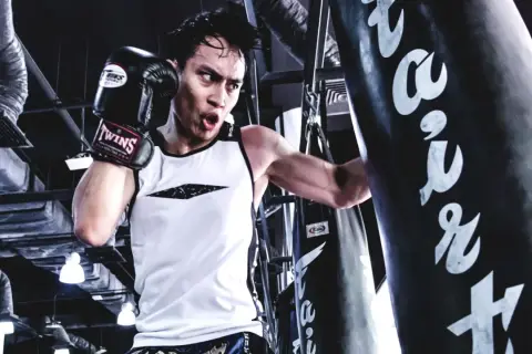 A boxer trains intensely, focusing on his boxing breathing as he punches a heavy bag.