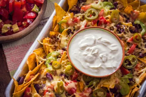 Nachos caseros con queso derretido, carne, frijoles, jalapeños y un tazón de crema agria.