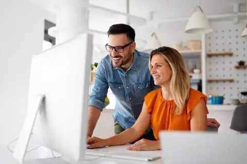 Coppia sorridente davanti al computer, scopre come funziona la banca ore per ottimizzare il lavoro.