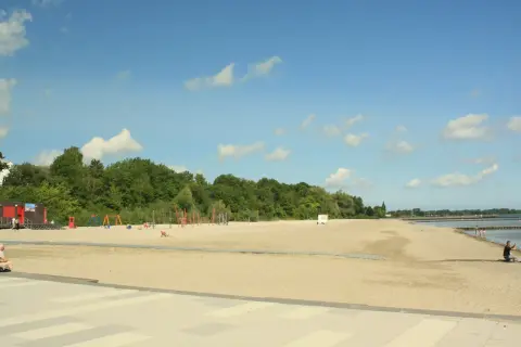 Sonniger **Stralsund Strand** mit Spielplatz, Liegewiese und Blick aufs Wasser. Ein Mann macht ein Foto.
