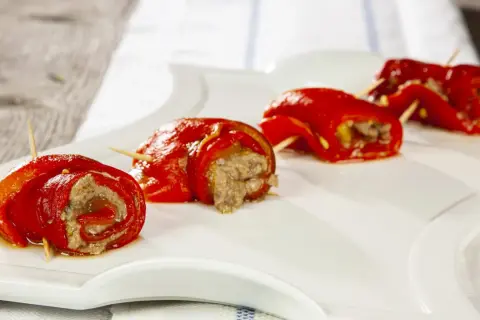 Peperoncini ripieni alla piemontese, rotolini rossi con ripieno saporito, serviti su un piatto bianco.