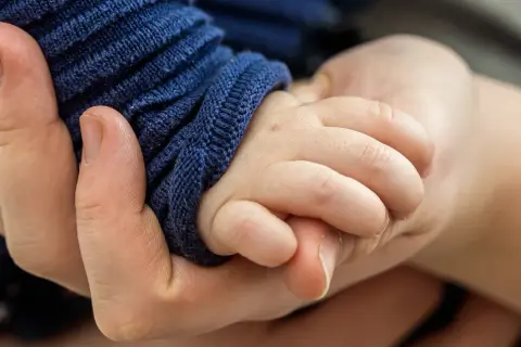 Eine Hand hält zart die kleine Hand eines Babys. Die Frage, warum hilft Gott nicht bei Depressionen, hallt in dieser Geste der Verbundenheit wider.