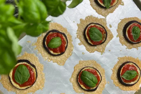Kleine Aubergine-Pizza-Häppchen mit Tomatensoße, Käse und frischem Basilikum auf einem Backblech.